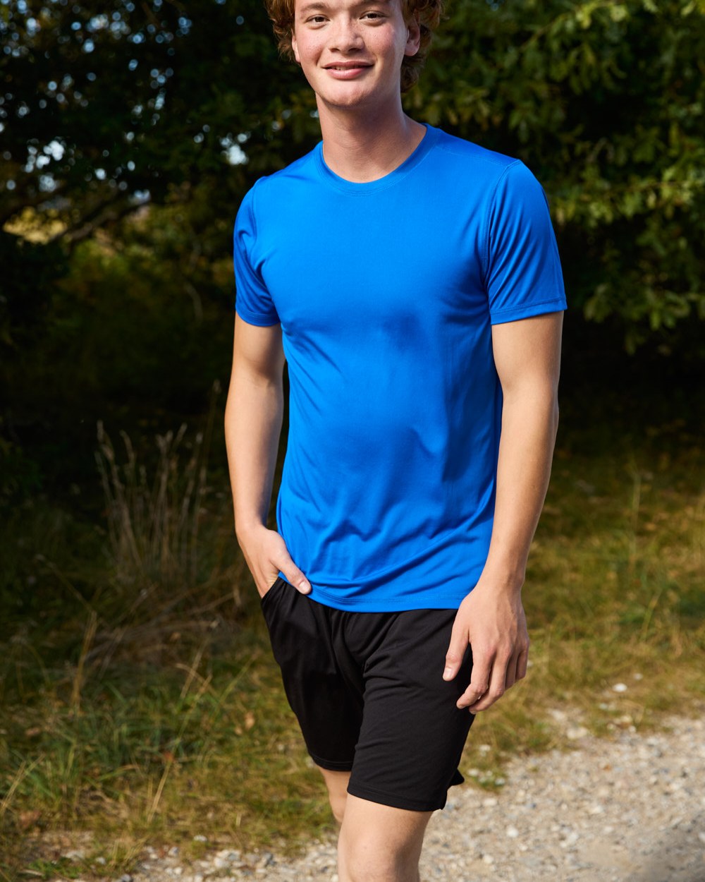 Model in blauem Recycled Performance T-Shirt und schwarzen Shorts